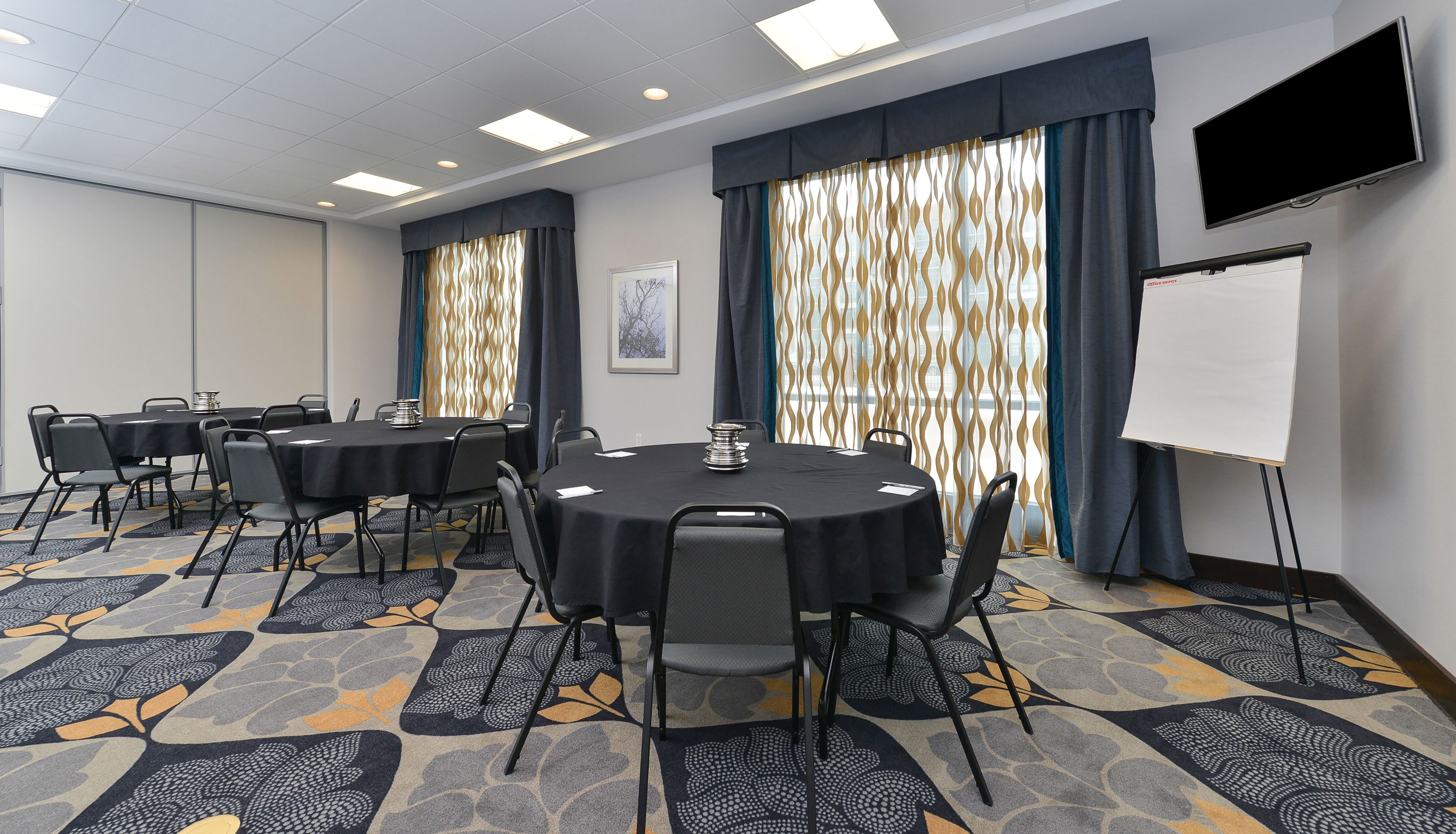 A conference room with round tables, chairs, a whiteboard, and patterned carpet.