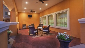 A covered patio area with wicker furniture, a ceiling fan, and large windows.
