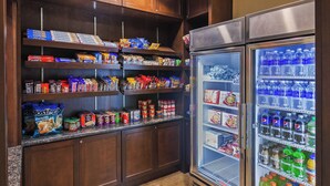 A kitchen with shelves stocked with snacks and a refrigerator filled with beverages.