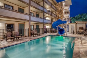 Una piscina de hotel con tobogán de agua, asientos al aire libre y un edificio de varios pisos con balcones.