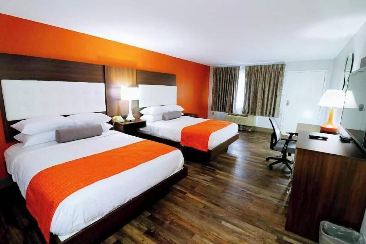 Une chambre d’hôtel avec deux lits, un bureau, une chaise et une fenêtre avec des rideaux.