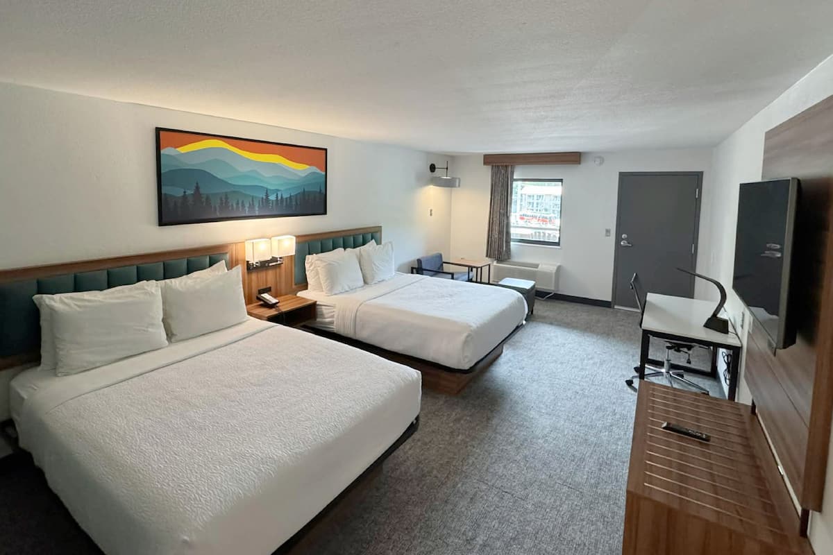 Une chambre d’hôtel avec deux lits, un bureau, une chaise, une télévision et un tableau au mur.