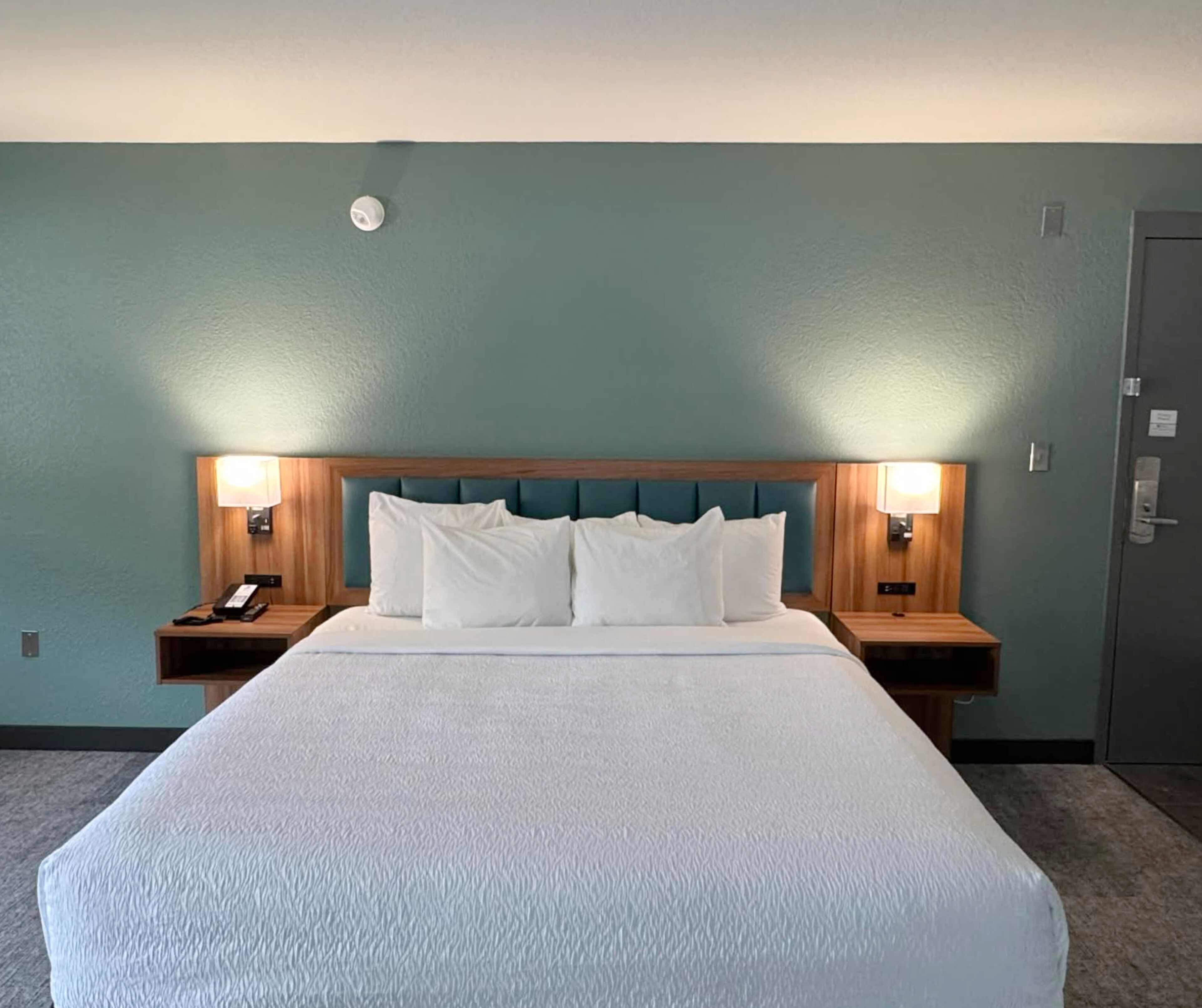 Une chambre d’hôtel avec un grand lit, deux tables de chevet avec des lampes, une tête de lit en bois et une porte.