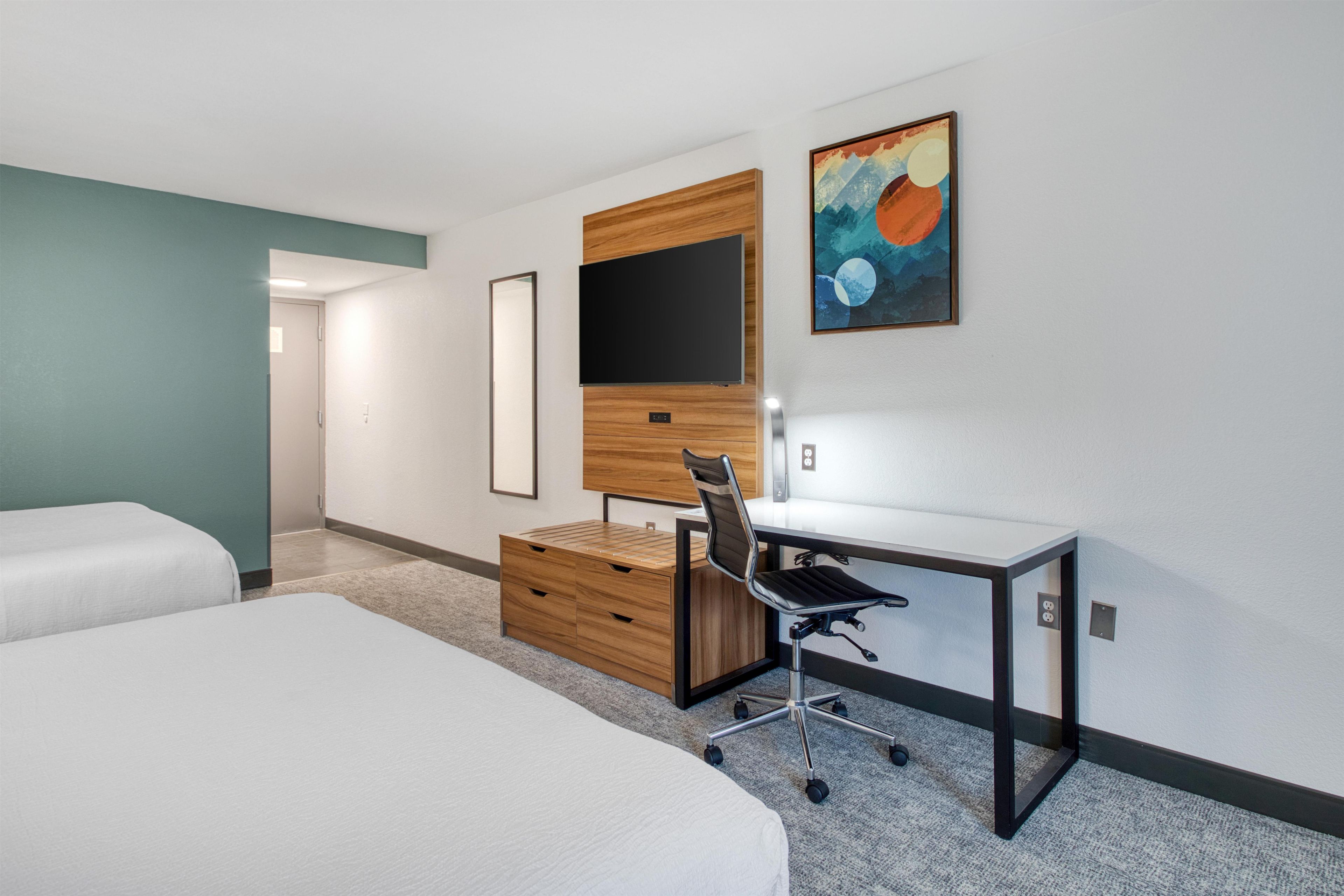 A hotel room with a bed, a desk with a chair, a flat-screen TV, and a painting on the wall.