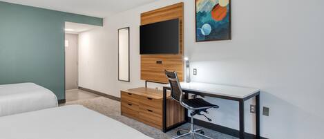 A hotel room with a bed, a desk with a chair, a flat-screen TV, and a painting on the wall.