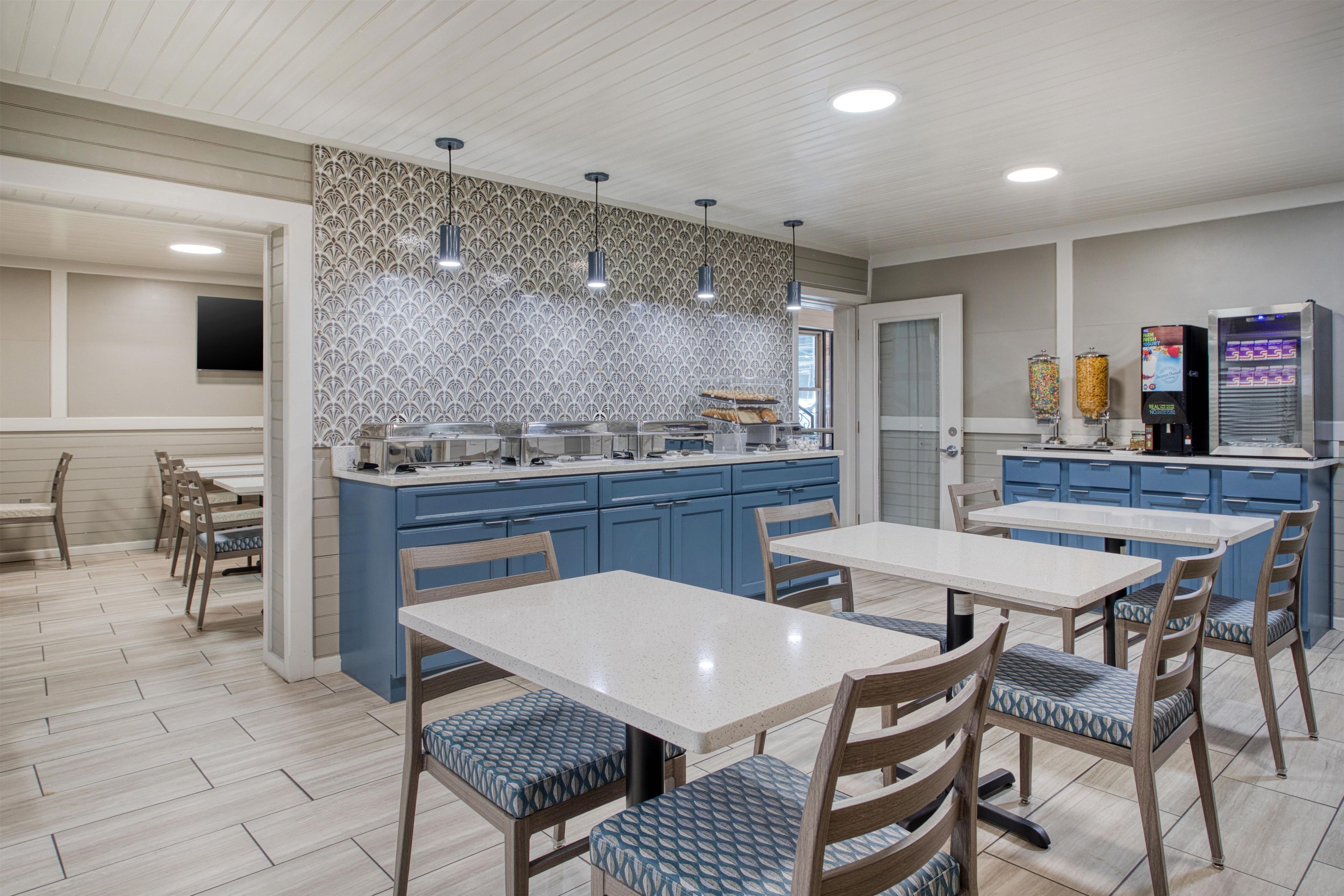 Une cuisine moderne avec des meubles bleus, un îlot central doté d’un évier et un bar pour prendre le petit-déjeuner. On y trouve également deux tables à manger avec des chaises.