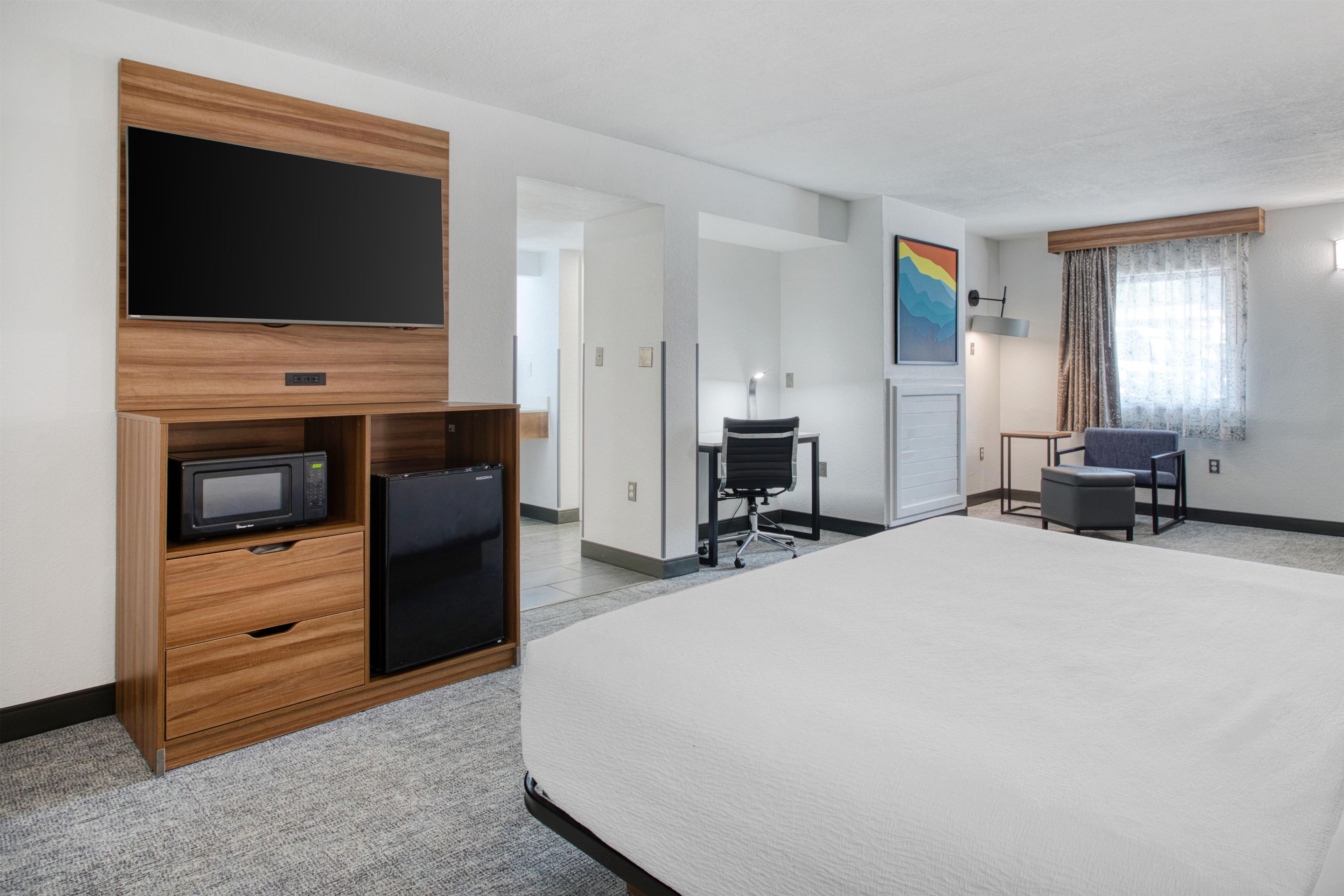 A hotel room with a bed, a desk with a chair, a television, a refrigerator, and a microwave.