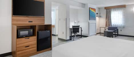 A hotel room with a bed, a desk with a chair, a television, a refrigerator, and a microwave.