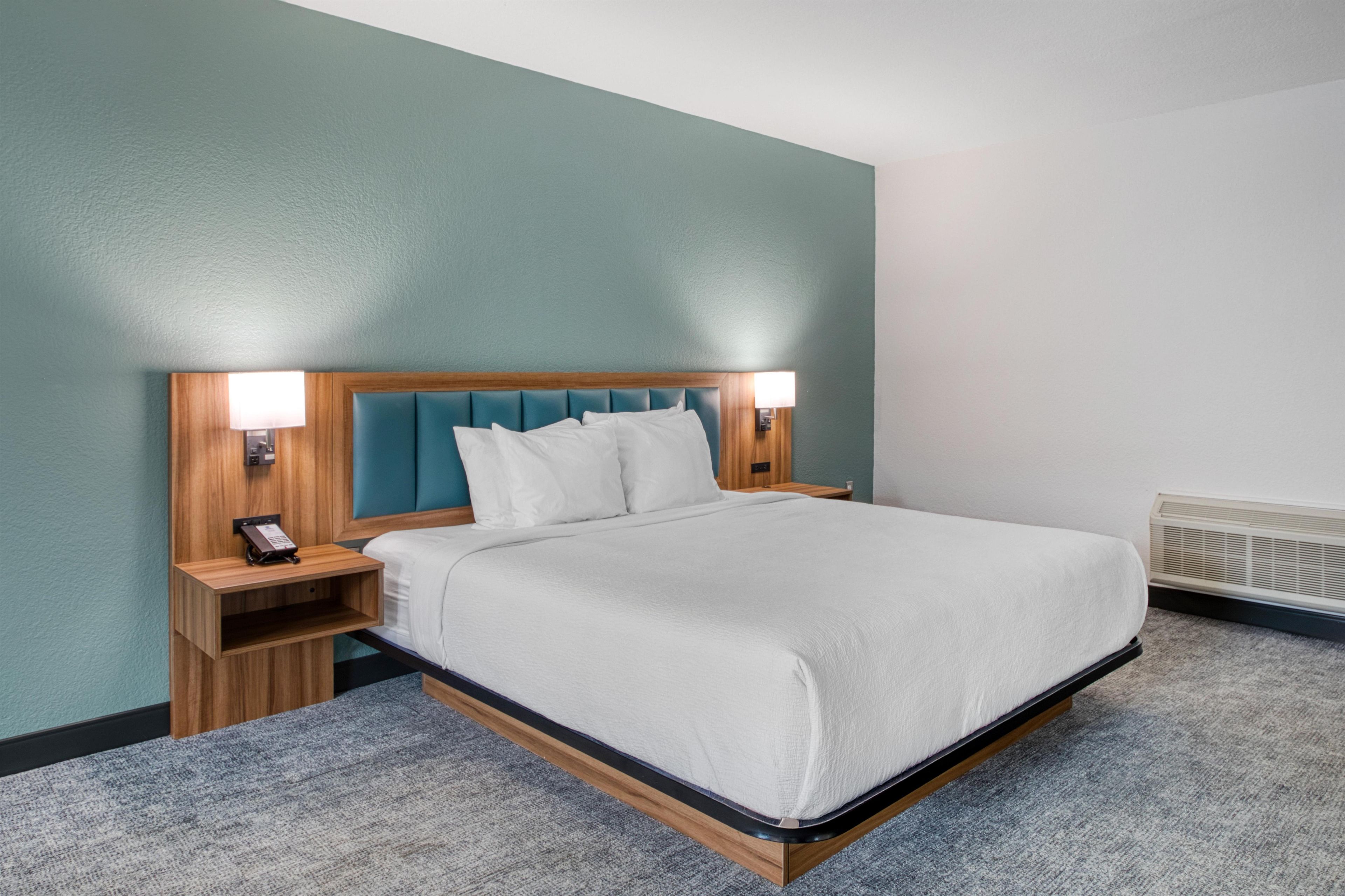 A hotel room with a bed, nightstands, a telephone, and a wall heater.