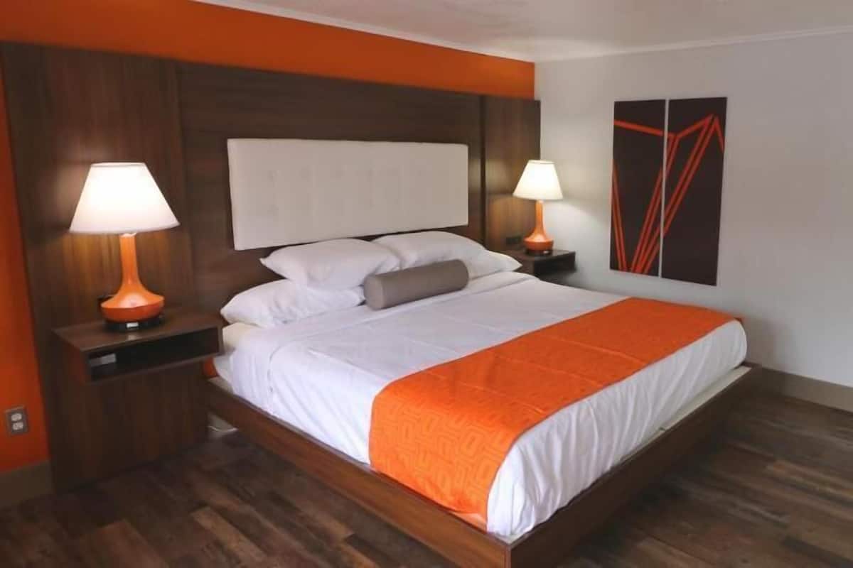 Une chambre d’hôtel avec un lit en bois, deux lampes de chevet, un grand tableau abstrait et un plancher en bois.