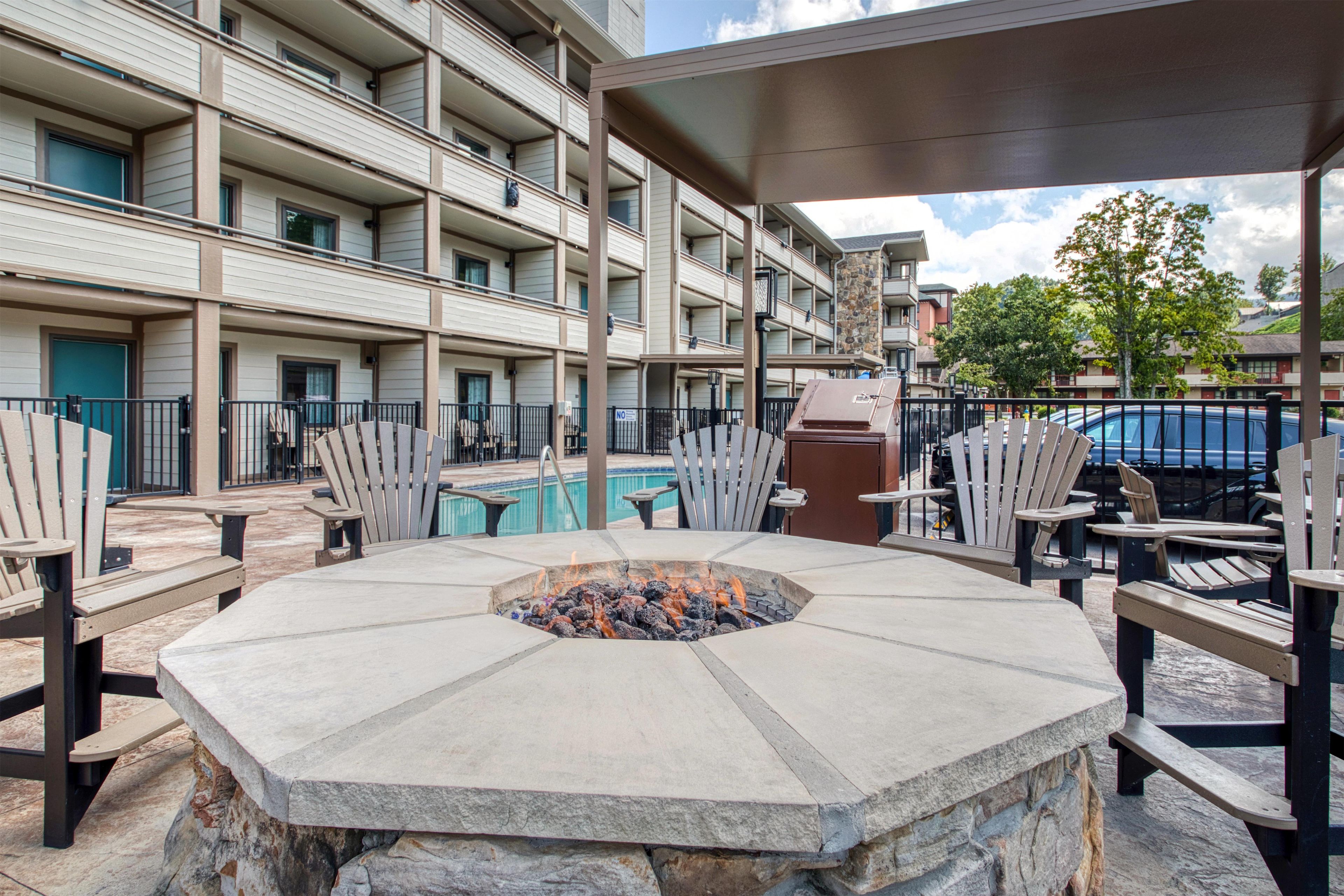A multi-story hotel with a pool area, outdoor seating, and a stone fire pit.