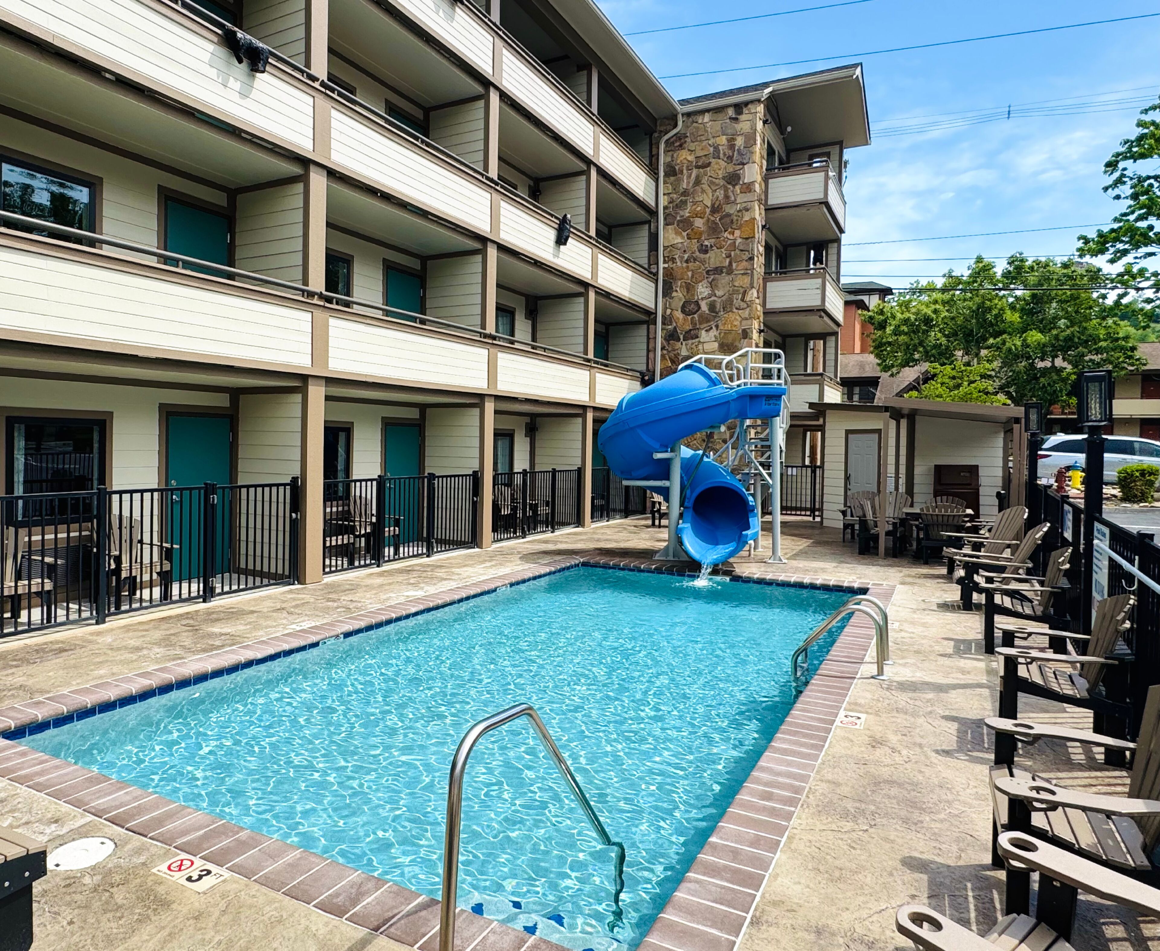 A swimming pool with a blue slide, surrounded by a multi-story building with balconies.