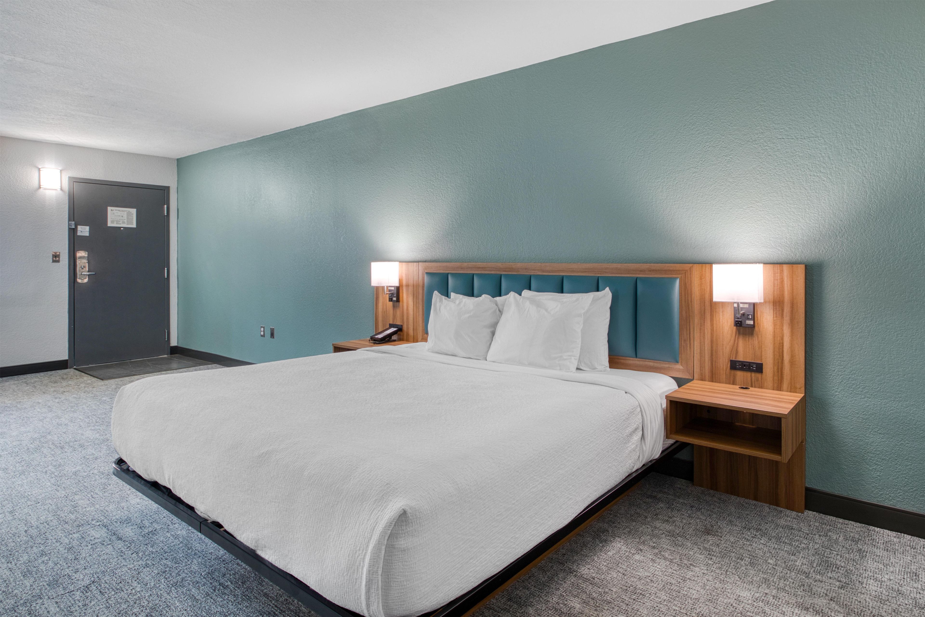 Una habitación de hotel con cama, mesitas de noche, una lámpara y una puerta.