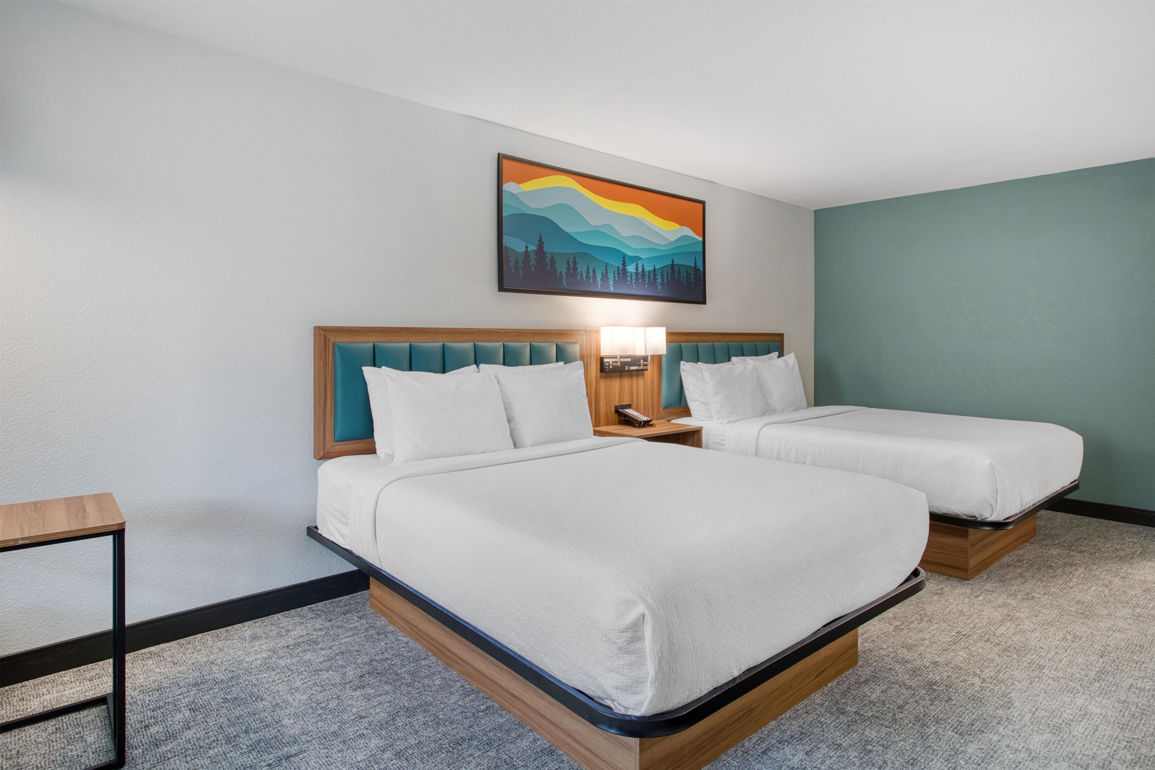 Een hotelkamer met twee bedden, een nachtkastje, een lamp en een schilderij aan de muur.