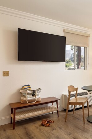 Une pièce dotée d’un téléviseur à écran plat fixé au mur, d’un banc, d’une chaise, d’une table et d’une fenêtre donnant sur un paysage verdoyant.