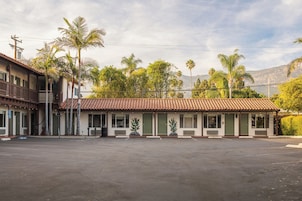 Um motel com telhado de azulejos, vários quartos e estacionamento.