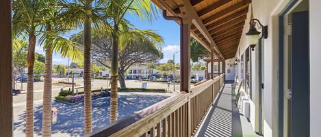 A balcony with a wooden railing overlooking a street with palm trees and parked cars.