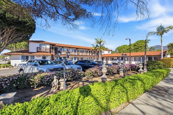 Un hotel amb teulades de rajola vermella, cotxes aparcats i jardineria cuidada.