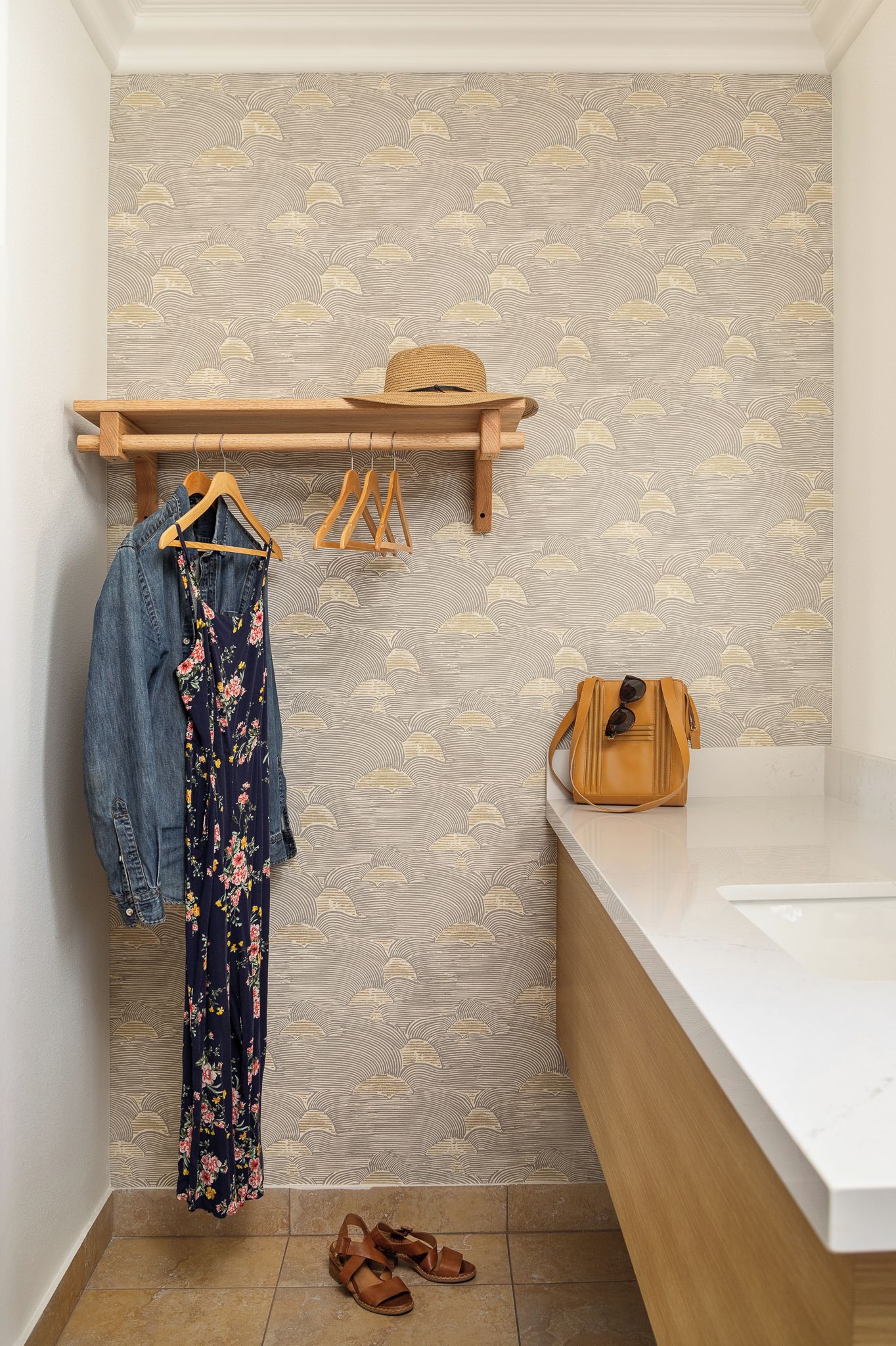 A bathroom with a wooden shelf holding a hat and a handbag, a floral dress, and a pair of sandals.