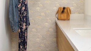 Un baño con un estante de madera que sostiene un sombrero, un bolso, un vestido floral y un par de sandalias.