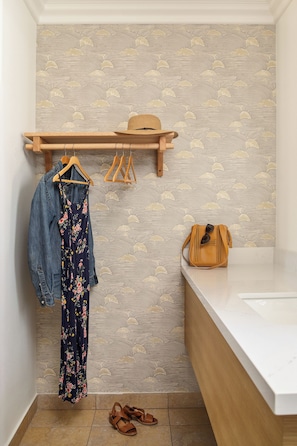 Une salle de bain avec une étagère en bois sur laquelle sont posés un chapeau et un sac à main, une robe à motifs floraux et une paire de sandales.