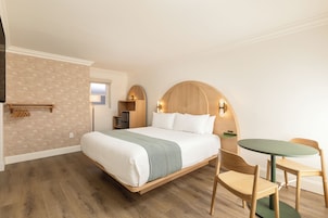 Quarto de hotel com cama, escrivaninha, cadeira e mesa pequena.