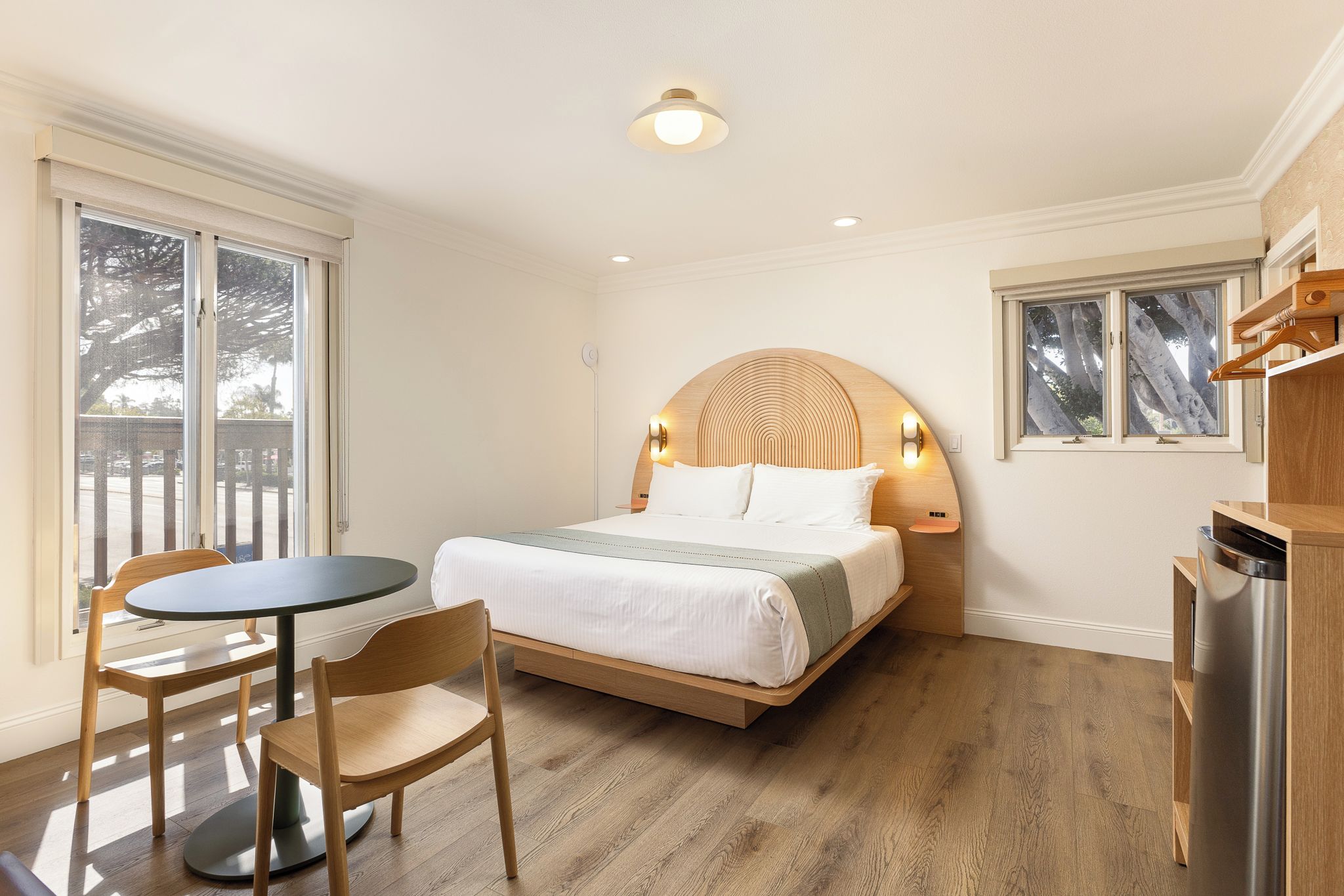 Quarto com cama, mesa, cadeiras e vista para o exterior.
