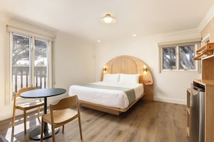 Quarto com cama, mesa, cadeiras e vista para o exterior.