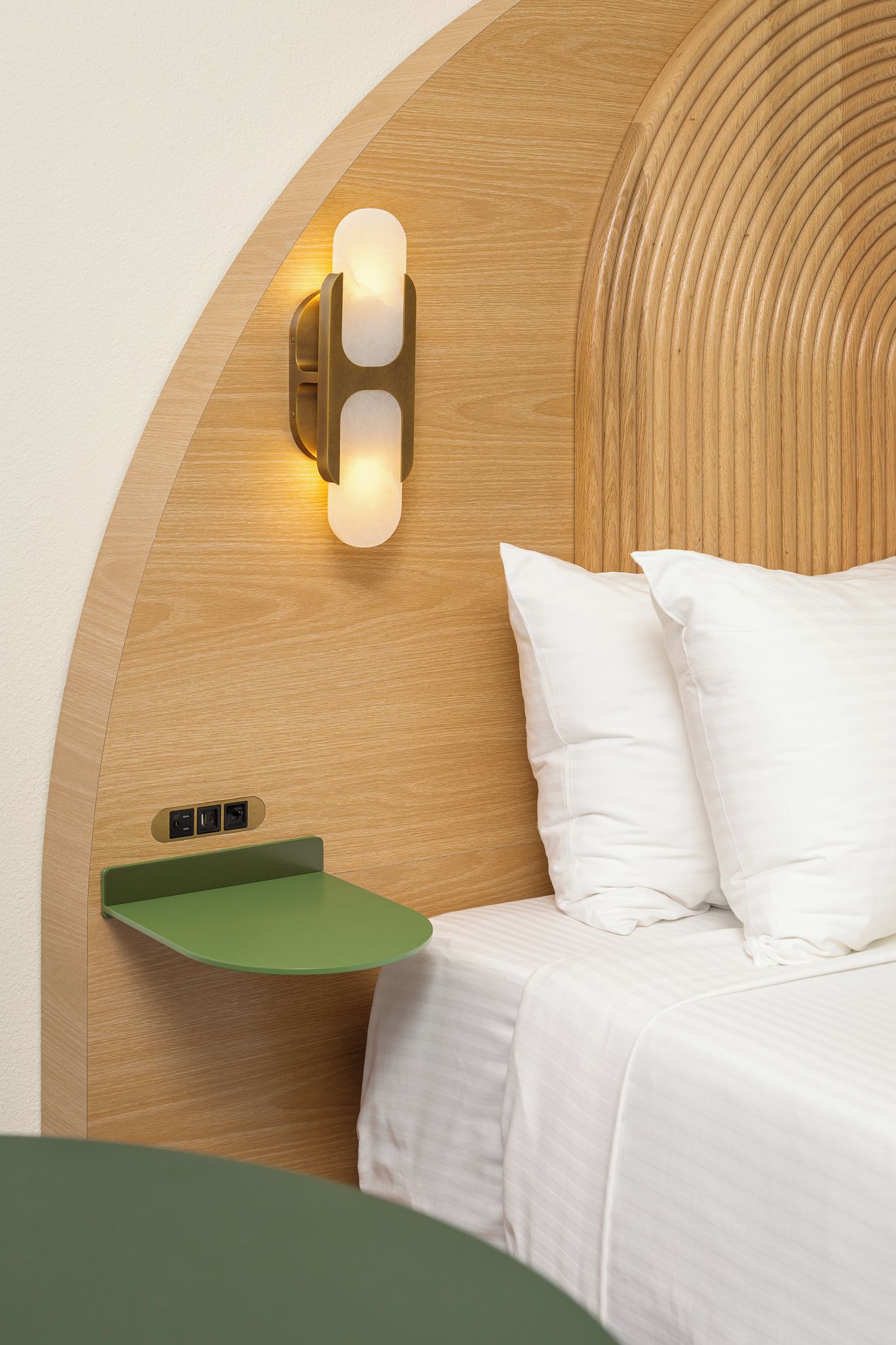 Un dormitorio con cabecera de madera, una mesita de noche con bandeja verde y una lámpara de pared.