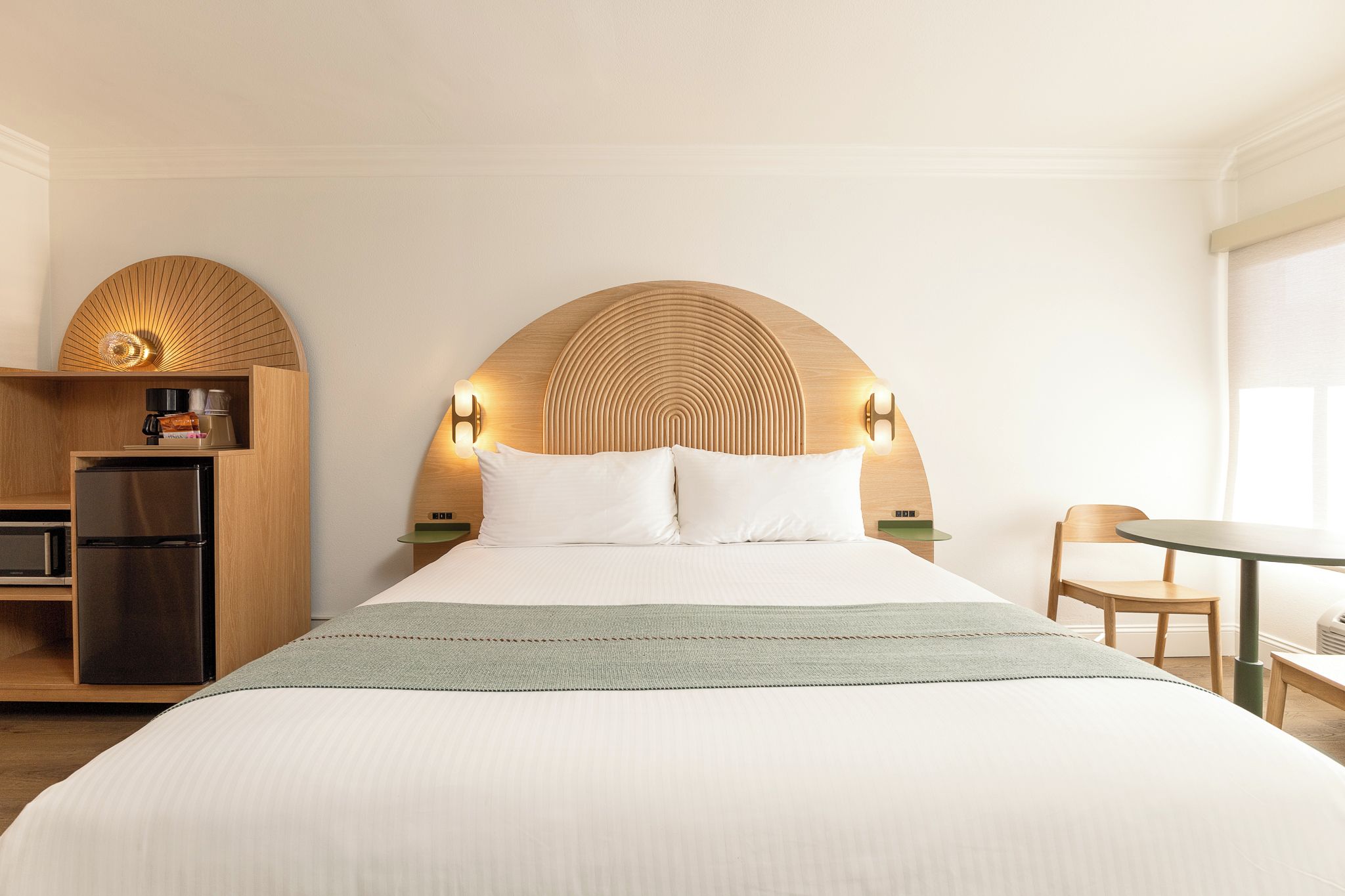 Una habitación de hotel con una cama grande, cabecera de madera, una kitchenette pequeña y un área de comedor.