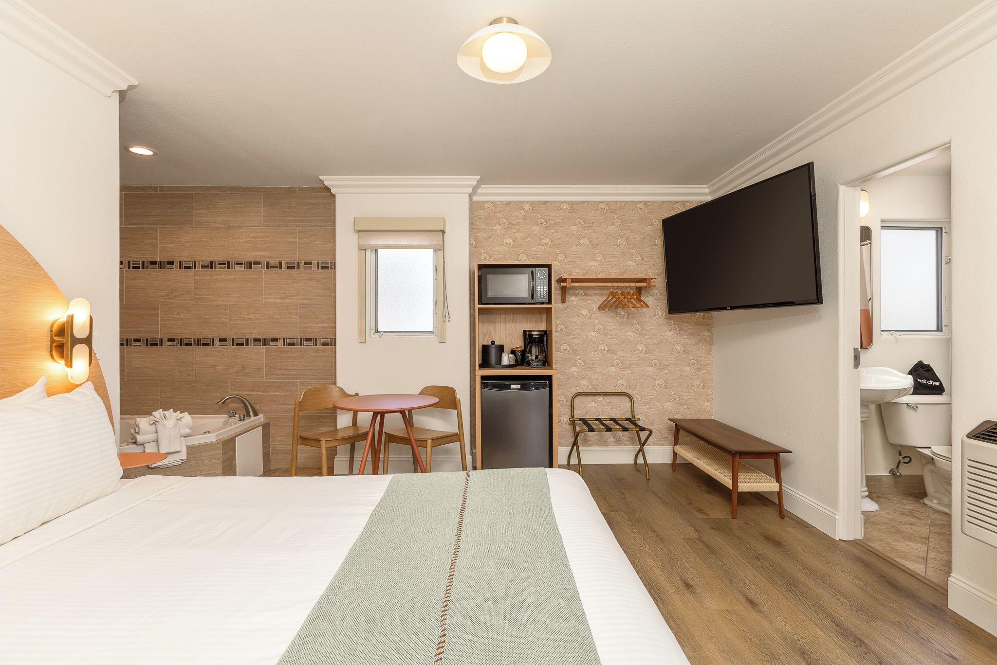 A hotel room with a bed, a desk, a chair, a television, a microwave, a coffee maker, and a small kitchenette.