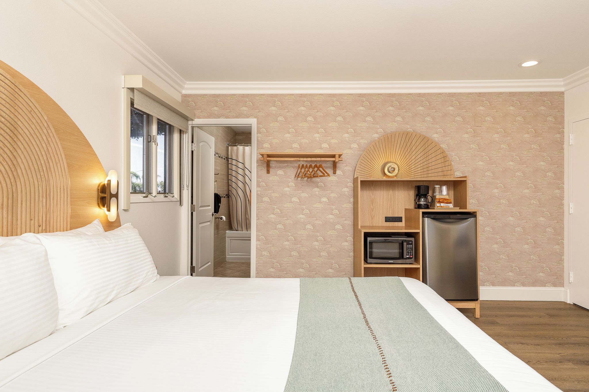 A hotel room with a bed, a small kitchenette, a microwave, a refrigerator, and a bathroom visible through an open door.