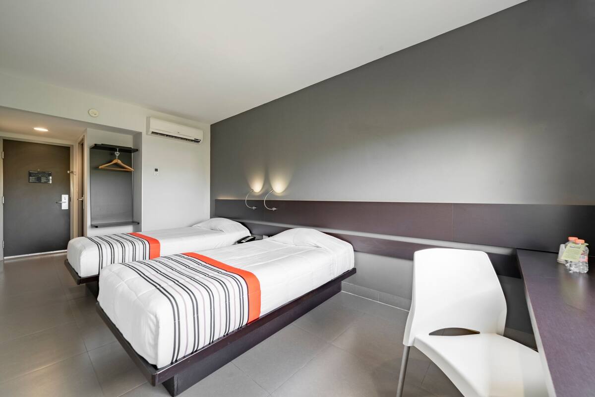 Une chambre d’hôtel avec deux lits, un bureau, une chaise et une armoire.