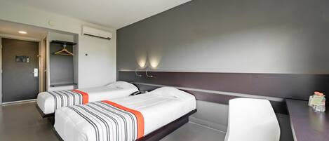 A hotel room with two beds, a desk, a chair, and a wardrobe.