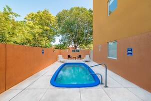 Una piscina con borde azul, rodeada por un muro de ladrillo bajo y dos sillas de descanso.