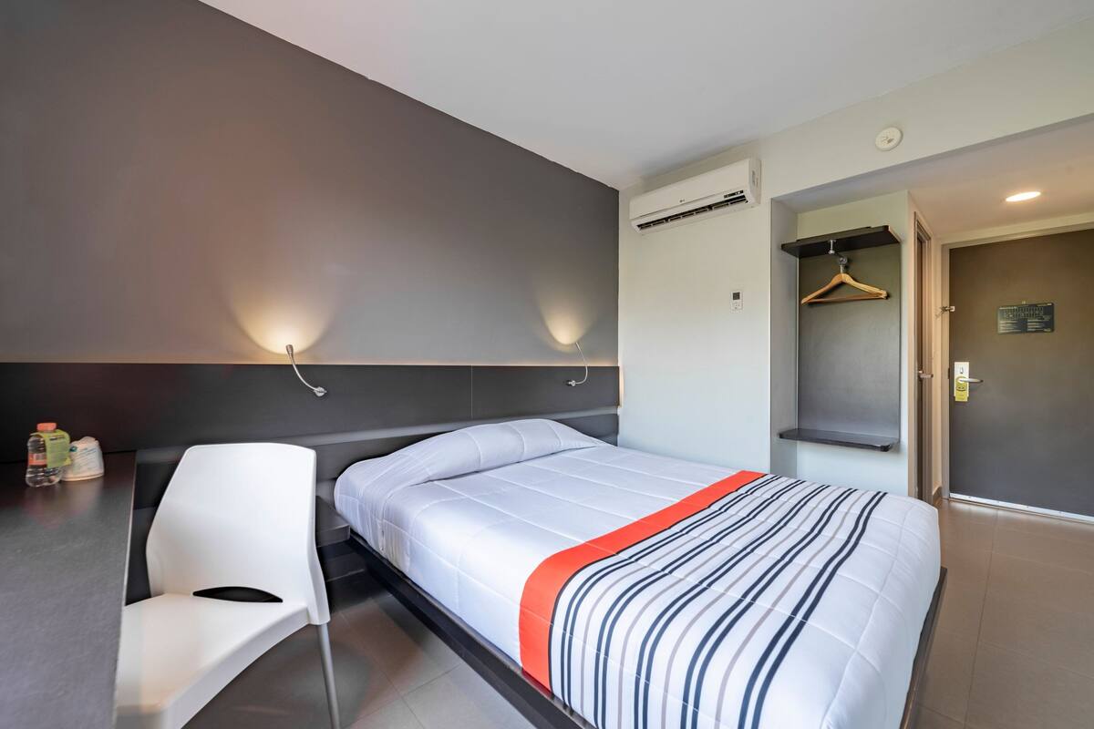 Une chambre d’hôtel moderne avec un lit, une chaise blanche, un bureau et une armoire.