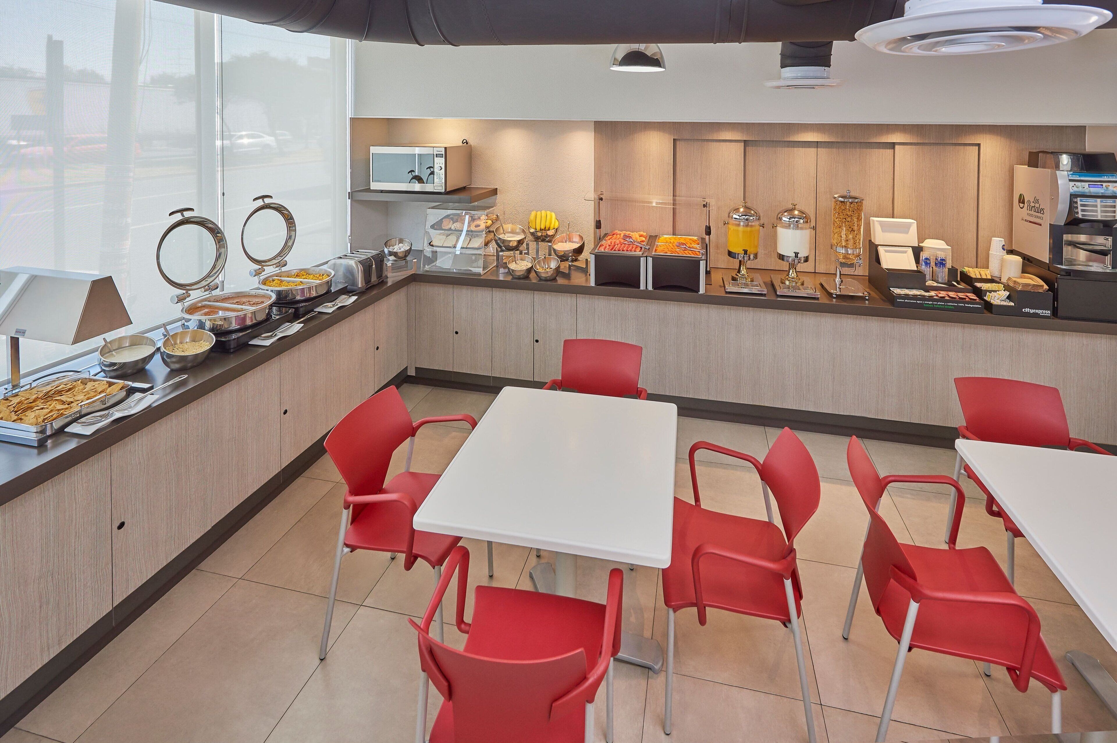 Zona de bufé para el desayuno con diversas opciones de comida, un microondas y arreglos de asientos.