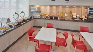 Zona de bufé para el desayuno con diversas opciones de comida, un microondas y arreglos de asientos.