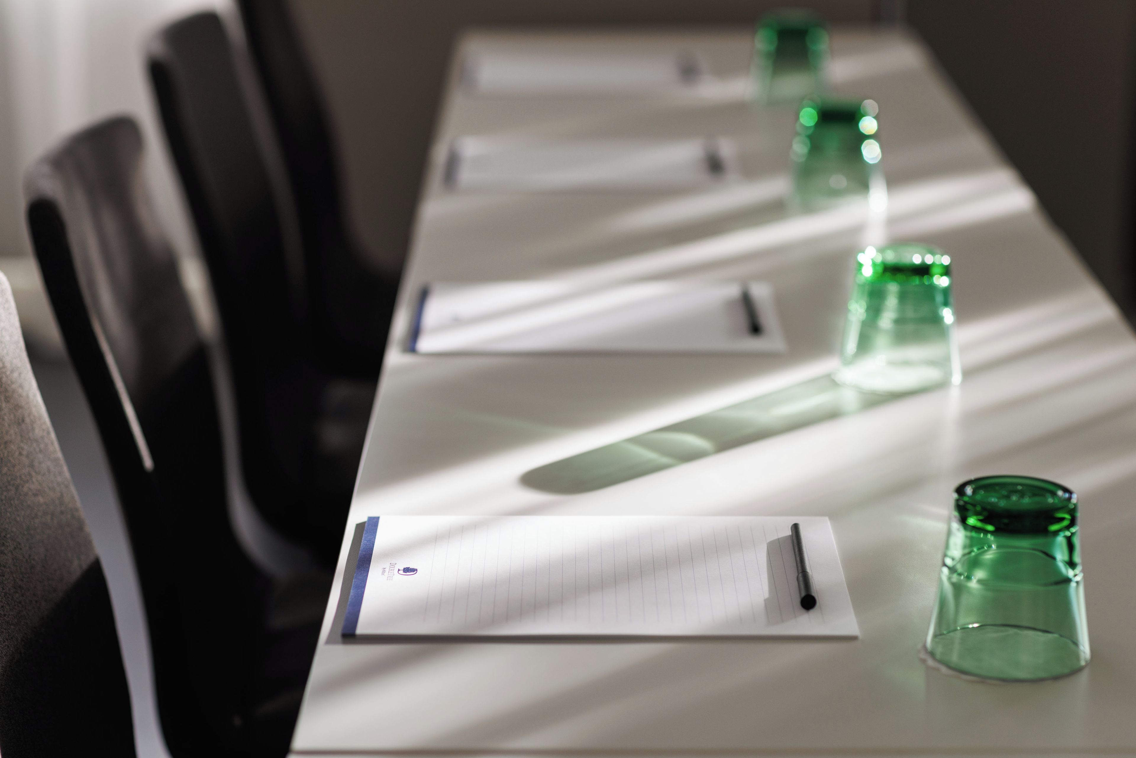 A conference table with documents, pens, and green glass bottles.