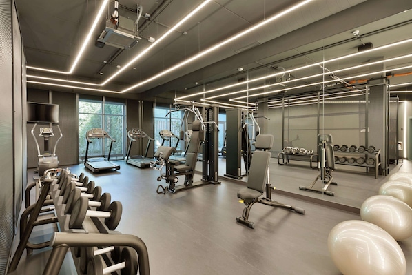 Un gimnasio moderno con diversos equipos de ejercicio, ventanas amplias y un diseño limpio y espacioso.