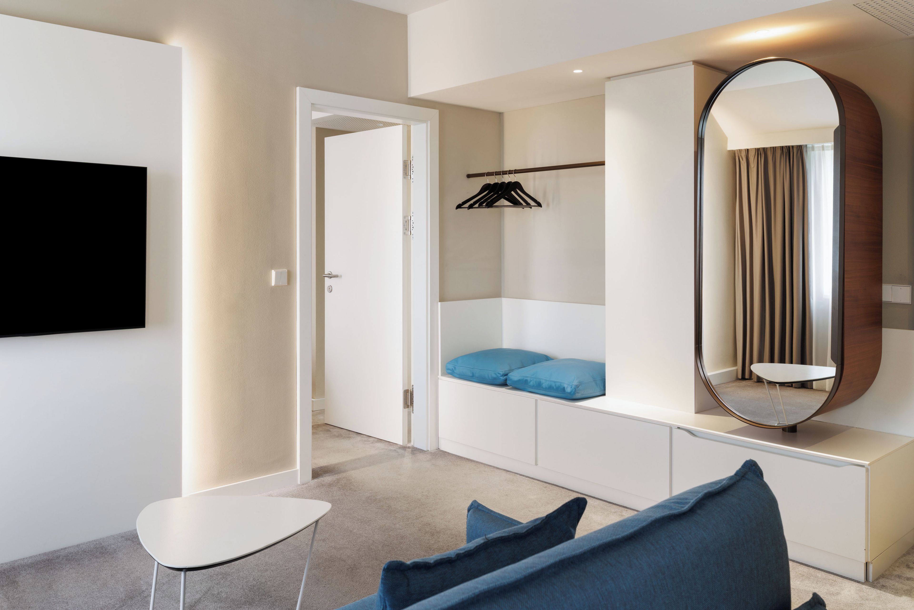 Un dormitorio moderno con una televisión de pantalla plana, un armario con espejo y una zona de estar con mesa y sillas.