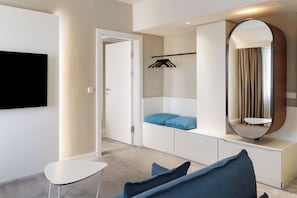 Un dormitorio moderno con una televisión de pantalla plana, un armario con espejo y una zona de estar con mesa y sillas.