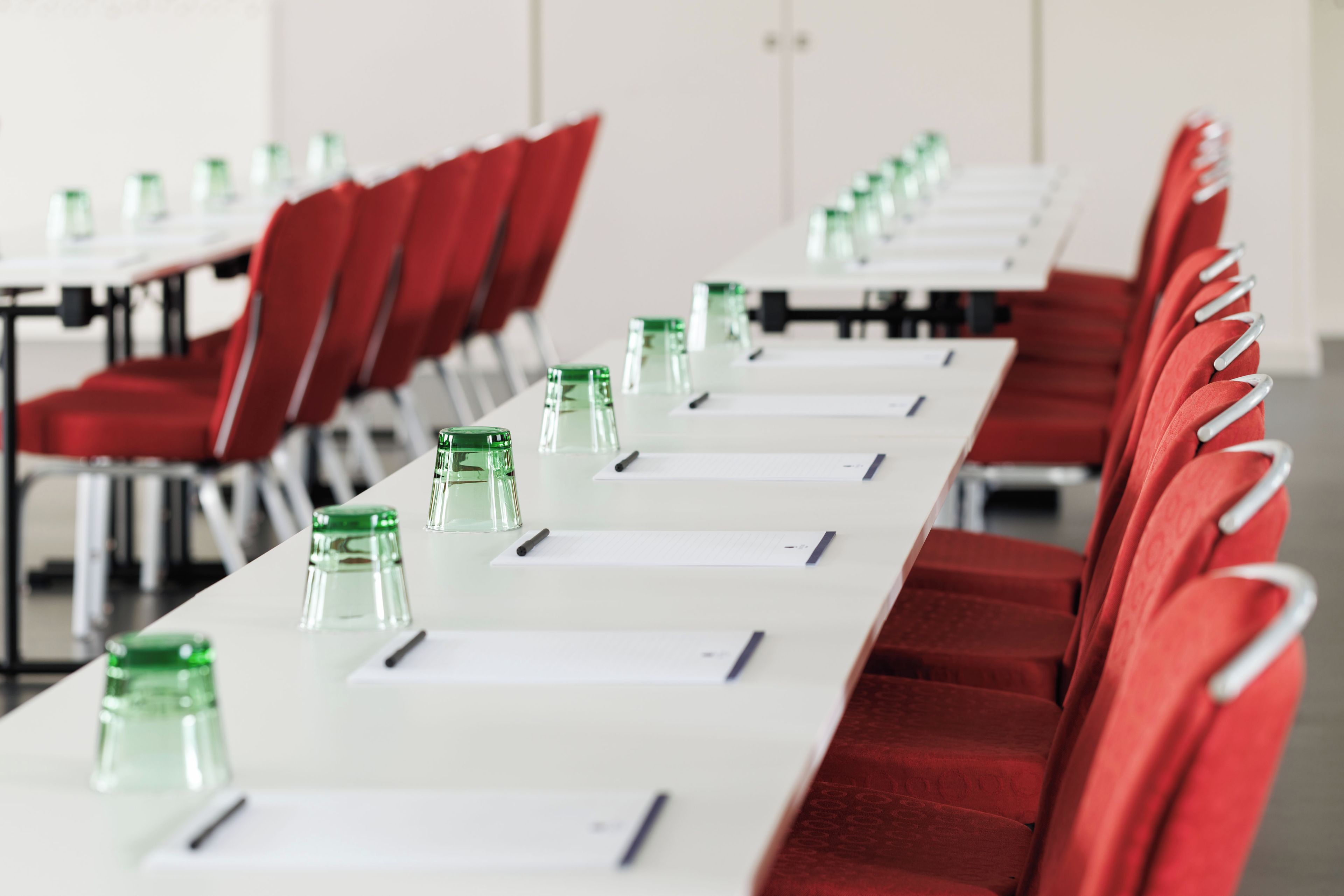 A conference room with rows of red chairs, white tables, and green water bottles.