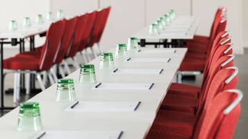 A conference room with rows of red chairs, white tables, and green water bottles.