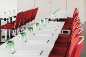 Un salón de conferencias con filas de sillas rojas, mesas blancas y botellas de agua verdes.