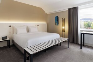 A hotel room with a large bed, bedside tables, a bedside lamp, a view of the outdoors, and a window with curtains. - DoubleTree by Hilton Vienna Bosei (Vienna)