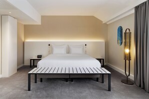 Habitación de hotel con una cama grande, mesitas de noche, una lámpara de noche y una luz empotrada en la pared, y vistas a un edificio a través de una ventana.