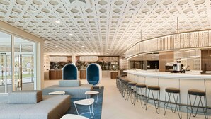 Un área de bar moderna con una barra curva, taburetes y un espacio de estar con sofás y mesas.