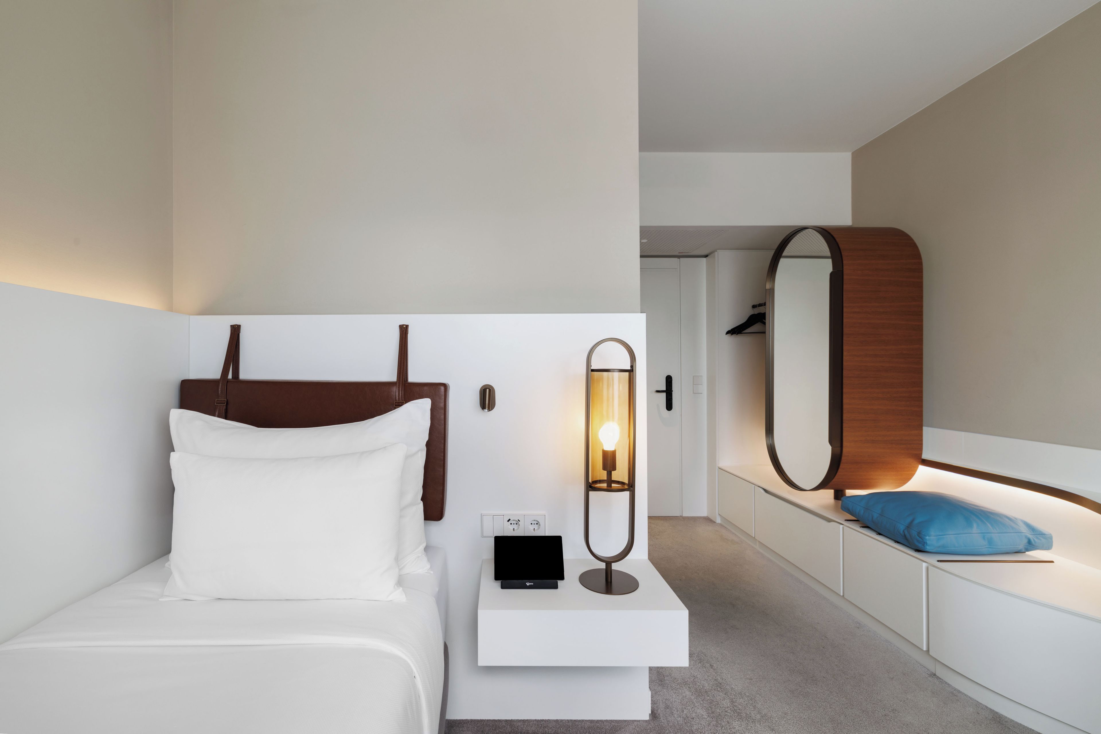 Ein modernes Hotelzimmer mit Bett, Nachttisch, Lampe und Spiegel.