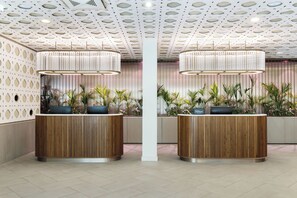 A hotel reception area with two wooden reception desks, a patterned ceiling, and potted plants. - DoubleTree by Hilton Vienna Bosei (Vienna)